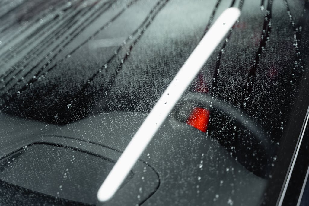 Close-up of a car windshield with water droplets creating an abstract pattern under light.