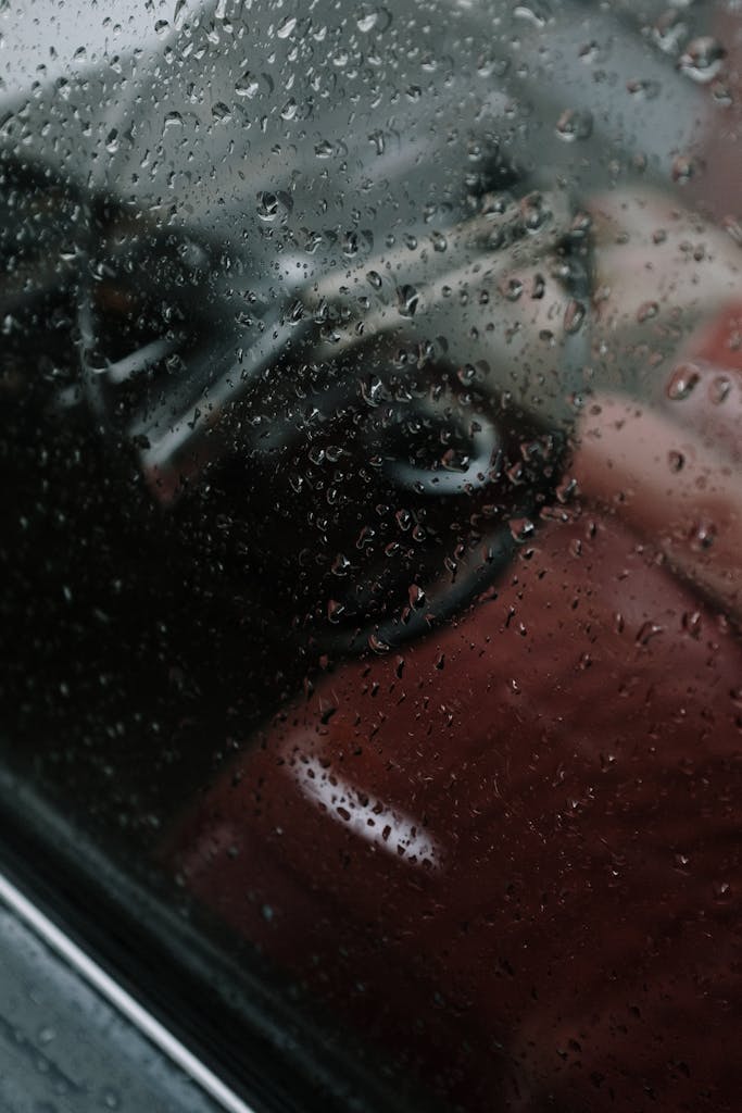 Close-up of a rain-soaked car window covered in water droplets, creating a textured glass surface.