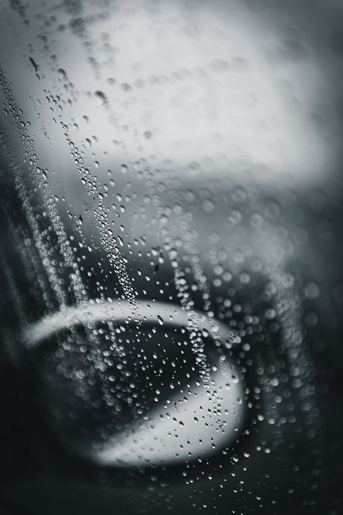 Close-up of raindrops on a car window, creating a blurred, moody effect.